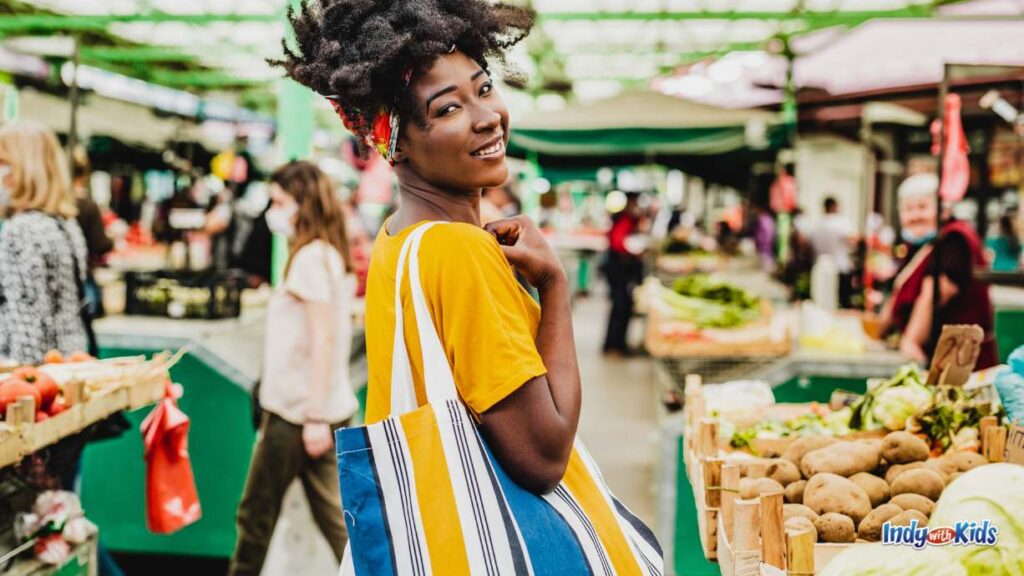 a woman looks back over her shoulder as she walks into a busy farmers market 