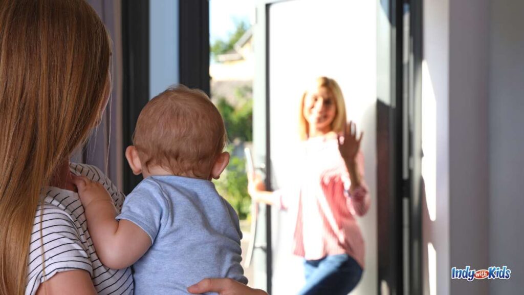 a mom waves to a baby who is being held by a babysitter as she walks out the door