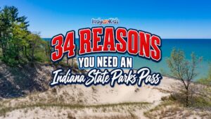 A sandy beach and bright blue lake shoreline at Indiana Dunes State Park with a graphic that reads “34 Reasons You Need an Indiana State Parks Pass.”