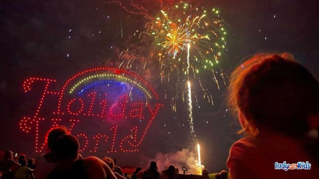 spectators watch fireworks at night with an LED Holiday World sign and rainbow lit up as well