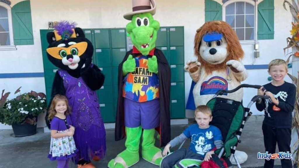 a little girl, a boy in a stroller, and another boy stand next to characters dressed up as a cat, dinosaur, and lion at Holiday World