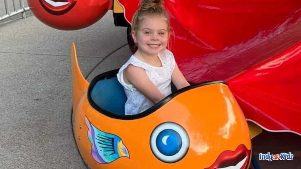 a little girl sits in a fish on a toddler ride