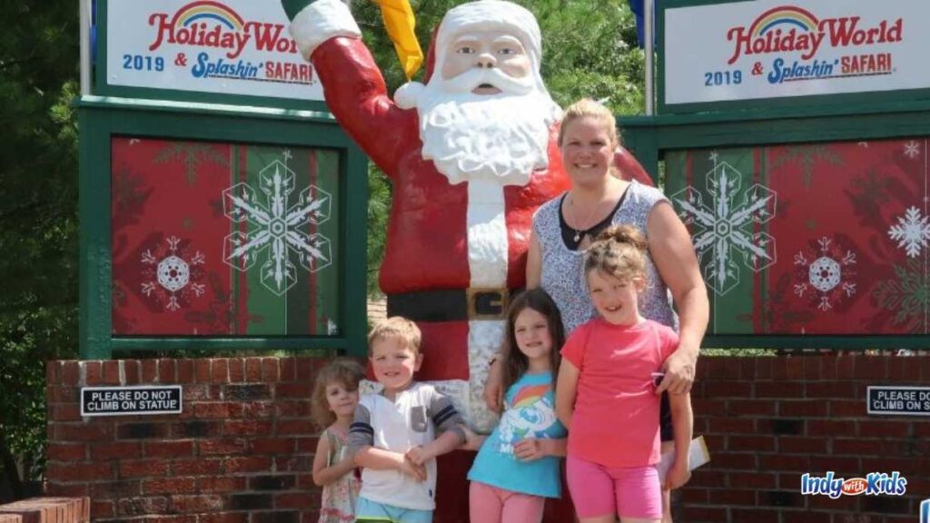 a mom and her three kids stand next to a santa Claus statue at the entrance of holiday world & splashin' safari