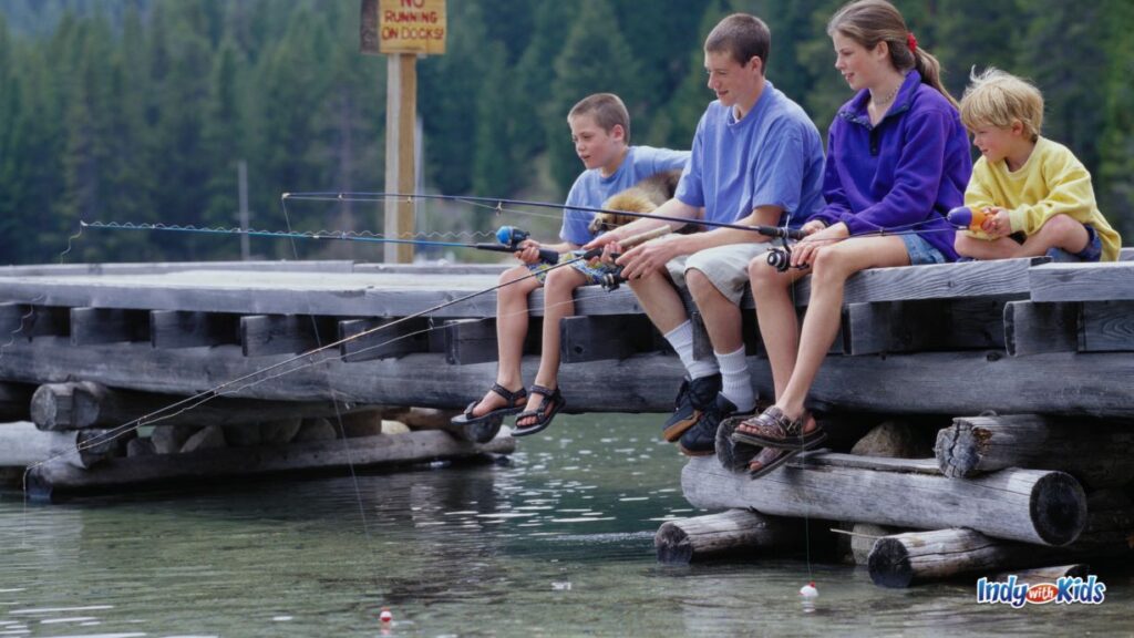 where to go fishing near me: two younger kids and two older kids sit on a pier with their feet hanging off over the water fishing.