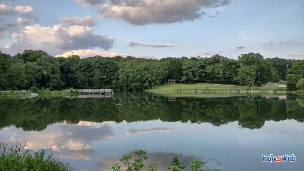 delaware lake pond with clouds in the sky reflecting on the water. there are trees and a bridge in the background.