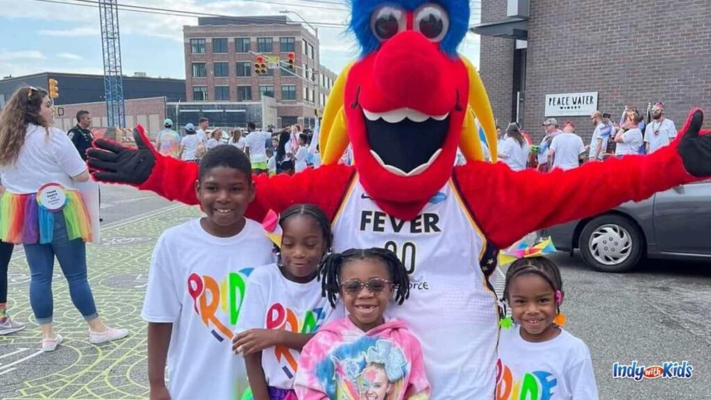 four children in pride gear stand in front of the Indiana fever mascot in downtown Indianapolis at the Indy pride festival