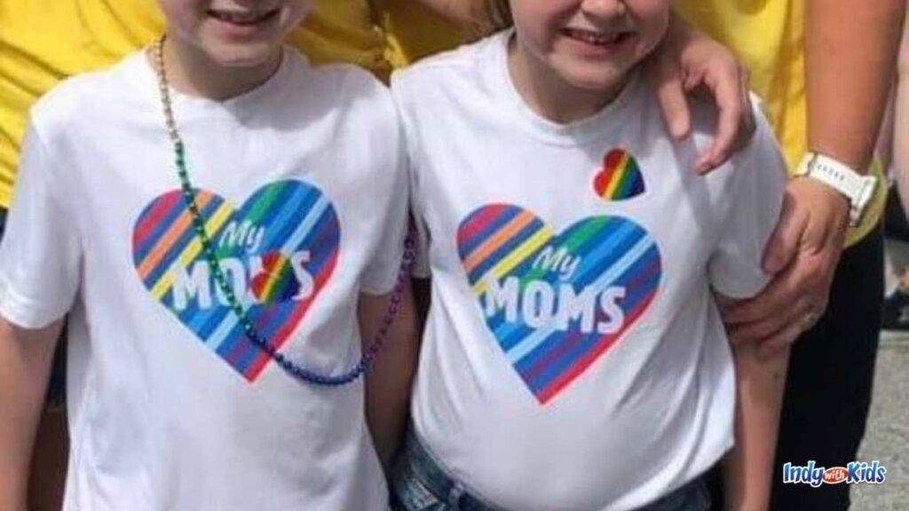 two children are wearing white t shirts with a rainbow heart. inside the heart is says my moms.