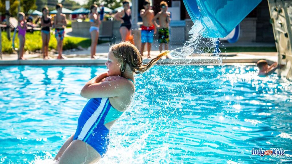 a girl in a blue swimsuit with her arms crossed over her chest is shot out of a plunge slide into a pool at the Carmel Water park
