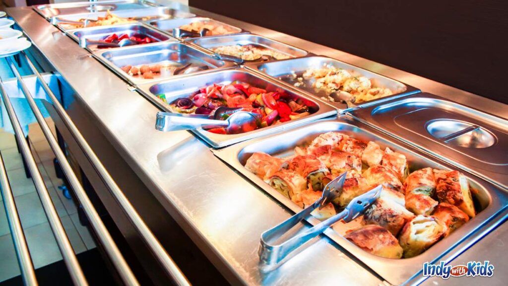 a cafeteria set up with all stainless steel counters and trays of food with tongs in each one to grab food.