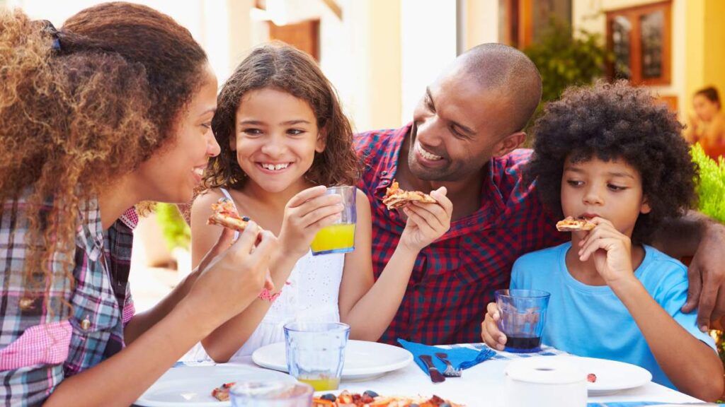 a mom, dad, a girl, and a boy gather together to enjoy pizza and orange juice