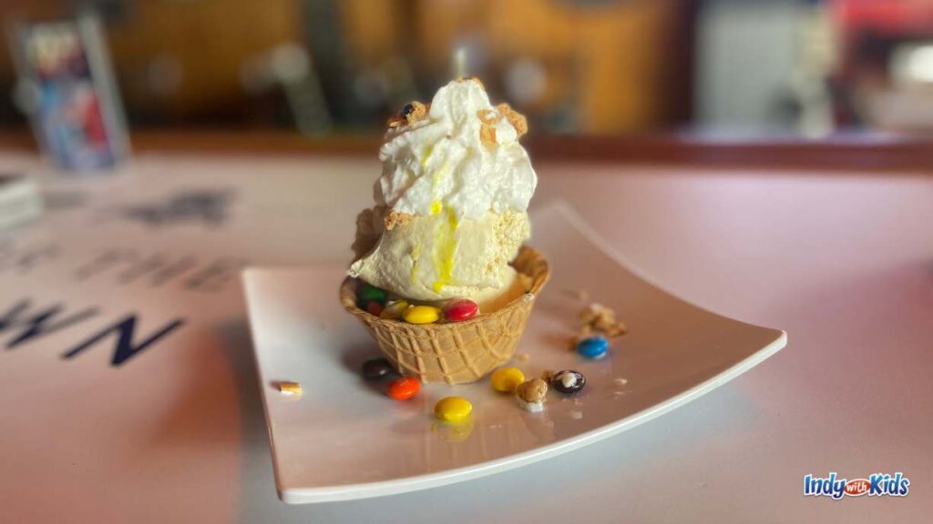 Spiked Shakes & Adult Slushies Near Me: on a square plate sits a cone cup topped with ice cream and whipped cream. M&Ms are sprinkled on the plate.