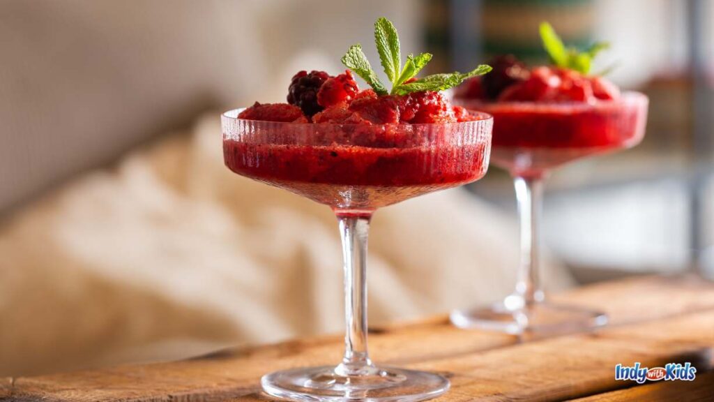 Spiked Shakes & Adult Slushies Near Me: a pretty red wine slushy is in a fancy shallow dessert glass topped with berries and mint leaves