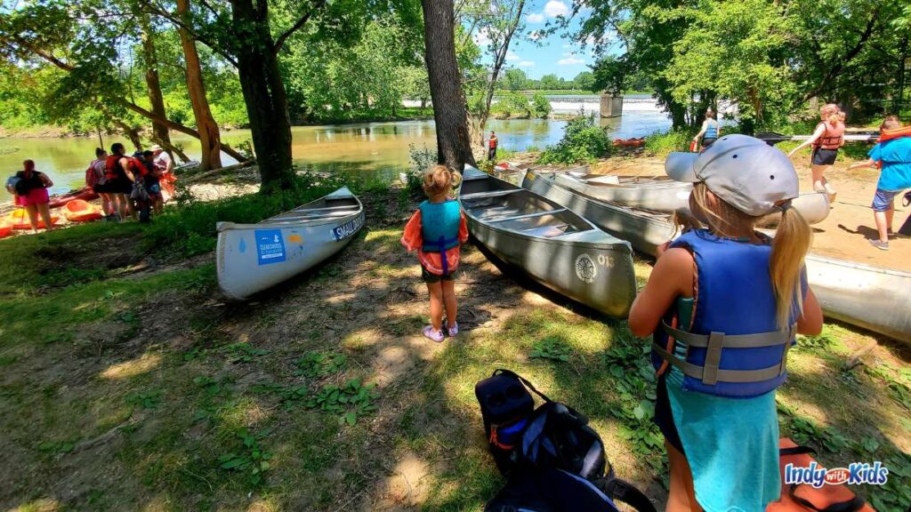 at a launch spot for the white River canoe company, there are several aluminum canoes waiting to be launched with kids and adults waiting their turn.