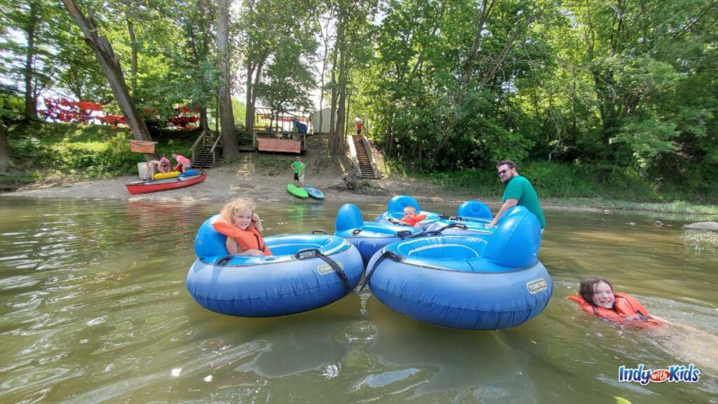 a man pulls in his group of 5 blue river tubes with kids in each tube. they are at the end of their white river canoe company excursion and are heading in to the red river livery.