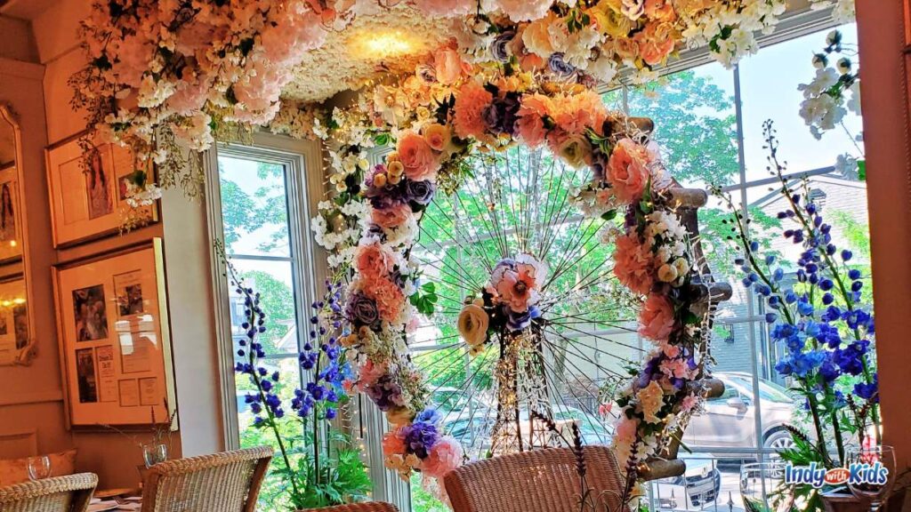 a beautiful wheel of flowers sits in the window at the Cake bake shop broad ripple. there are tons of flowers above the window as well.