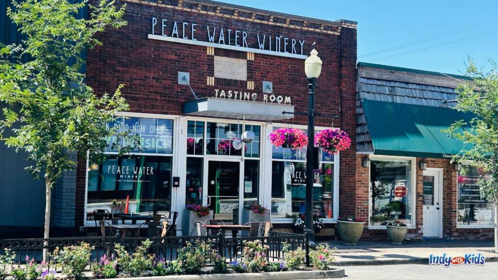 a view of the facade of peace water winery from across main street at the Carmel Arts & Design District. there are tables outside to sit at on the sidewalk and a sign that says 'tasting room' above the door.