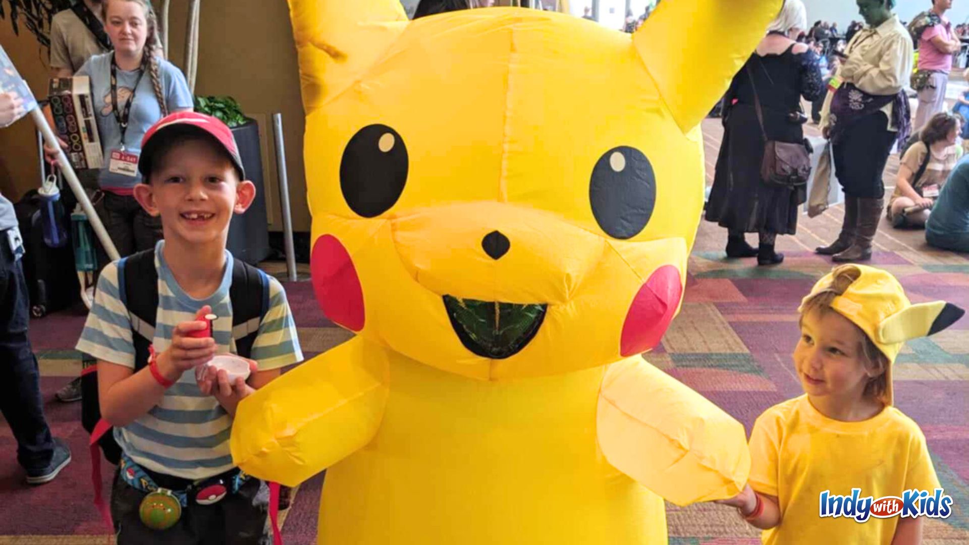 Gen Con With Kids: Two children pose with a person in an inflatable Pikachu costume.