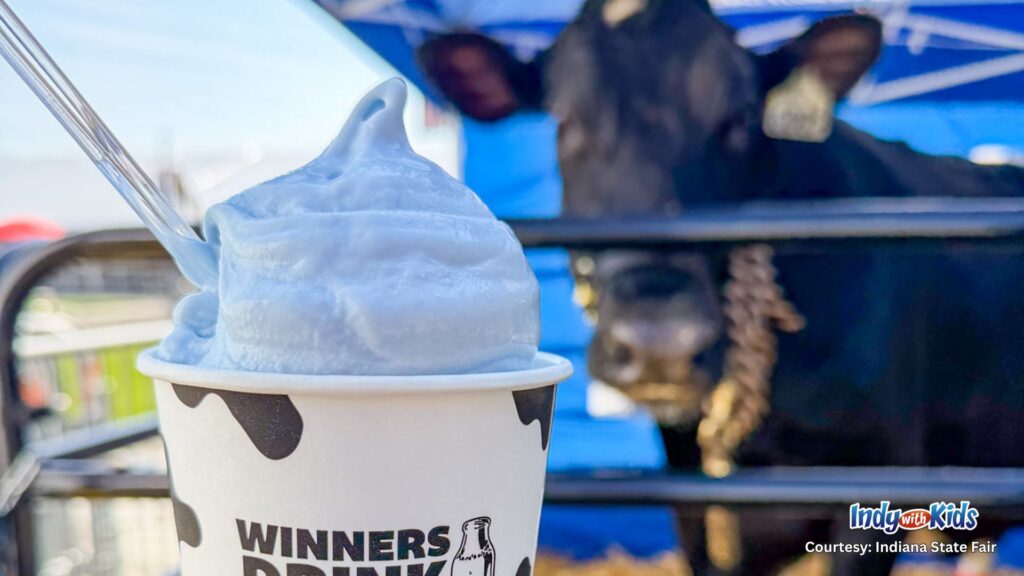 A cup of bright blue milkshake with a dairy cow blurred in the background.