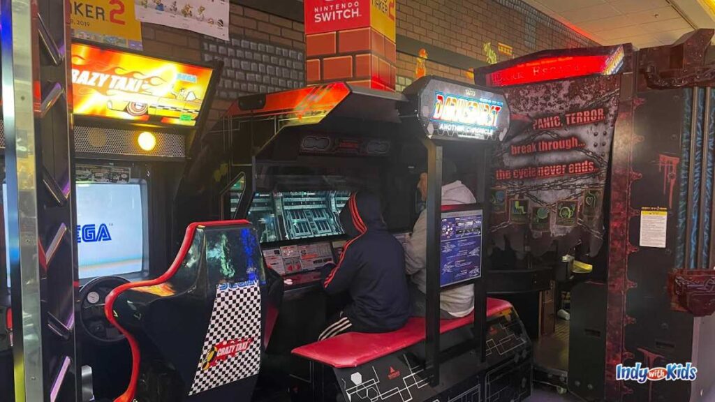 an adult and a child sit on a red bench and play an arcade game at Boss Battle Games