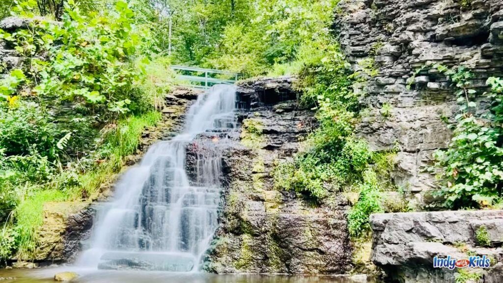 13 Fascinating Waterfalls in Indiana: water flows down limestone with lush greenery to its side and behind it