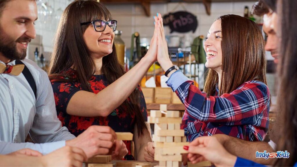 20 Great Things to Do in Indianapolis in November: two women high five around a table with lots of people playing jenga at a bar