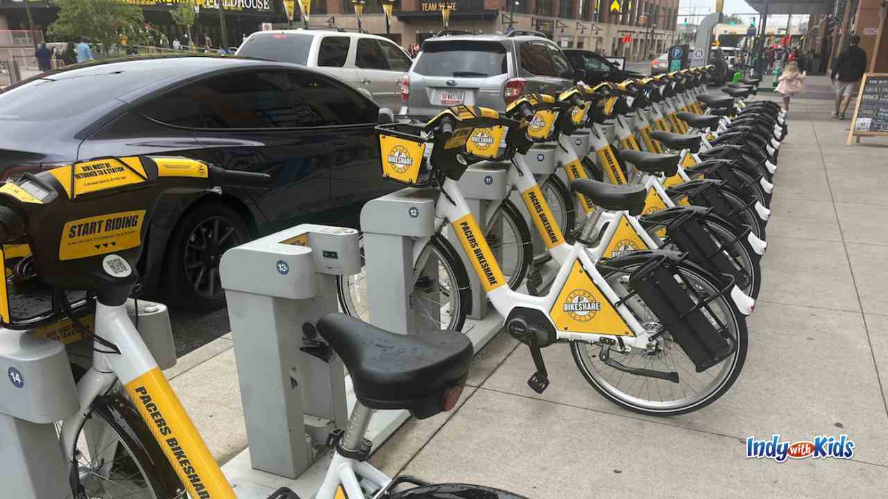 yellow white and black metal bike share bikes with baskets are parked along the sidewalk downtown