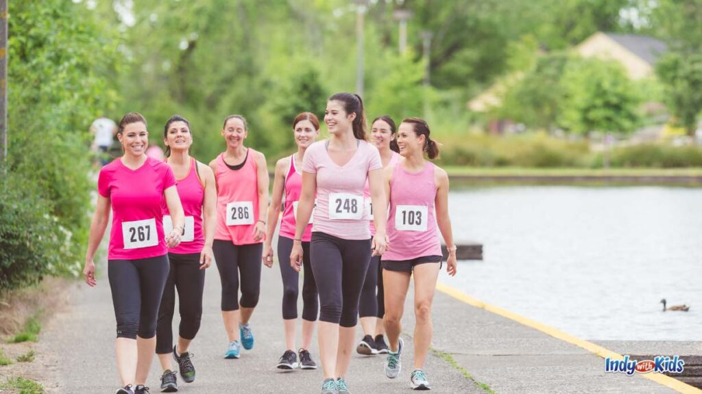 Holiday 5Ks in Indianapolis: Conquer Indy Turkey Trots & Christmas 5Ks - 7 women wearing pink walk with race bibs on them alongside a lake