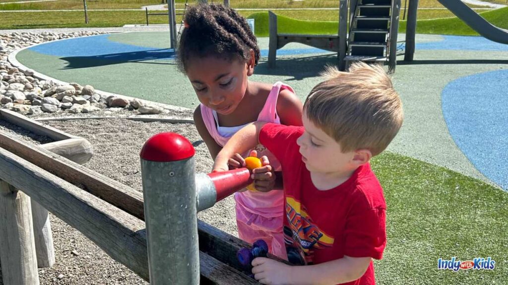 a boy and a girl play with a water table feature at Virgil Park, turning blue and yellow knobs on the wooden water table