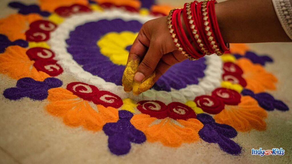 a woman's hand decorates a Diwali rangoli using colored sand