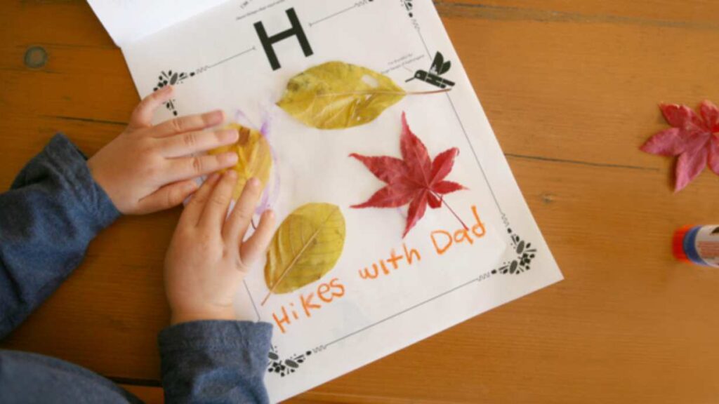 encouraging thankfulness: a child presses down a leaf onto a paper craft. there are other leaves glued on already and the words Hikes with dad written in crayon on it.