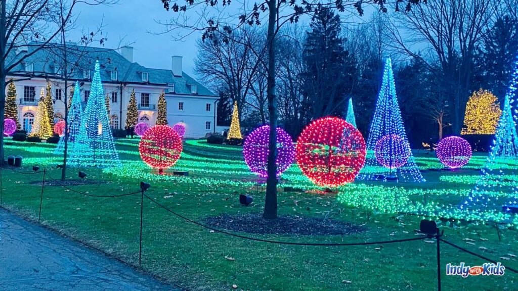 the lawn of the Lilly House at Winterlights at Newfields is covered with lit up trees and bushes of all different colors