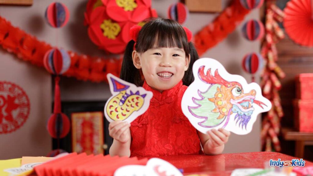 20 Cheap Things to Do in Indianapolis JANUARY EVENTS & ACTIVITIES: a little girl dressed in a red Chinese dress holds up two crafts in a room decorated all red with Chinese new year crafts