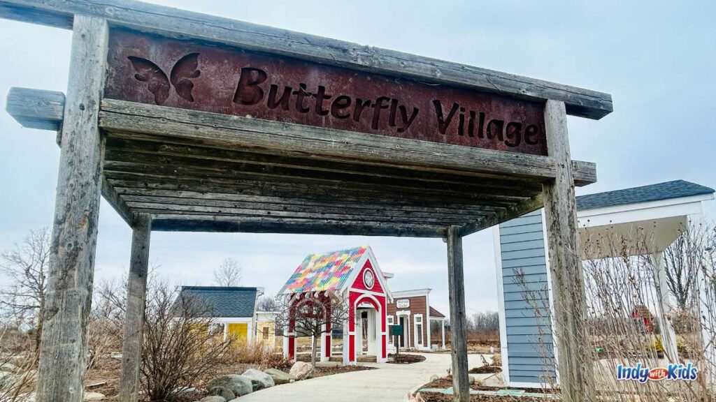 a sign that reads butterfly village leads to wooden storefronts for kids to explore in at coxhall gardens