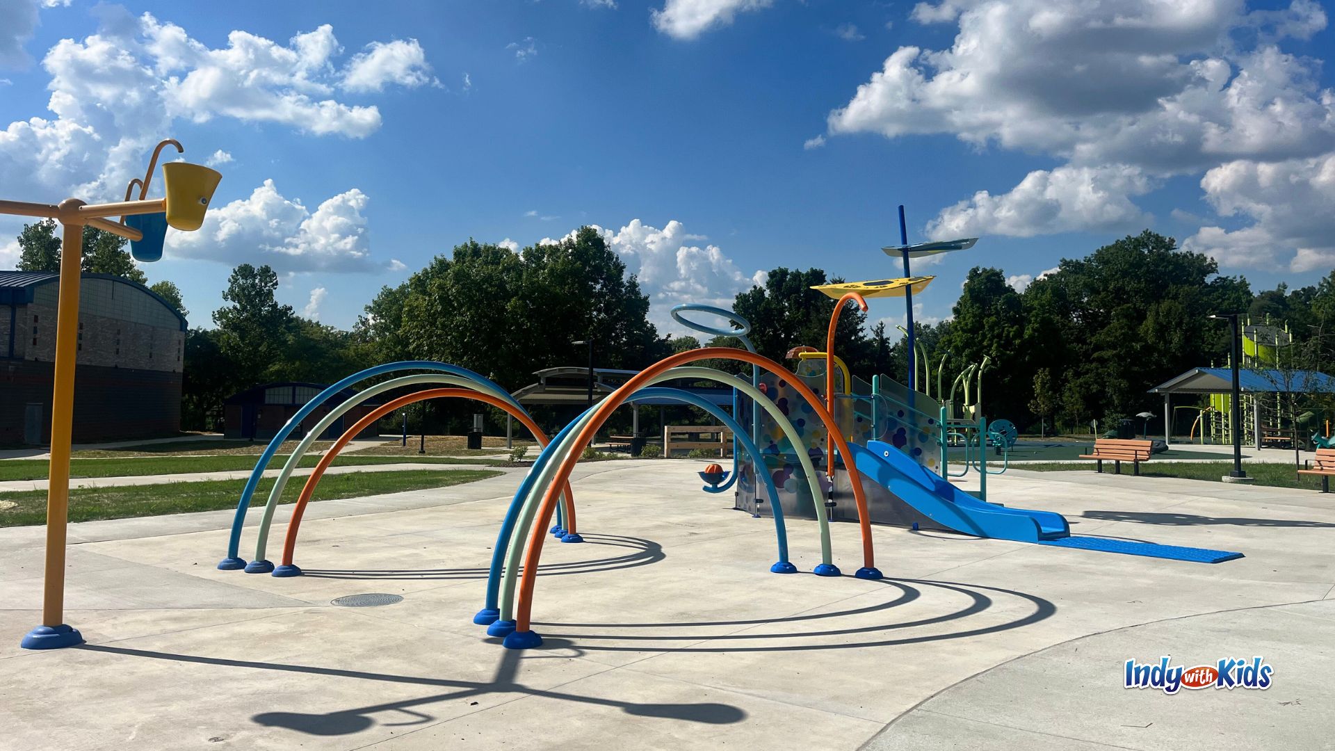 The splash pad at Washington Park in Indianapolis features rainbow spray features, a water slide, and dumping buckets.