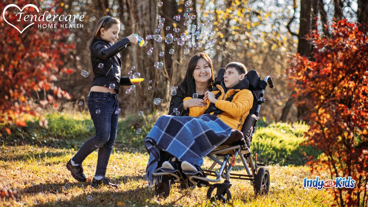 A girl blows bubbles near a woman kneeling by a boy in a wheelchair.