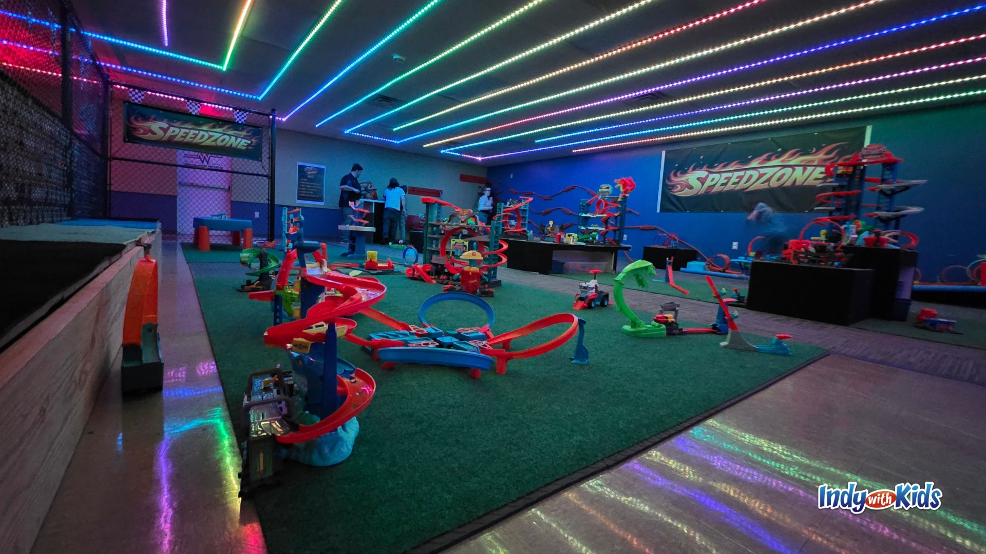 Low-angle view of SpeedZone indoor play area with Hot Wheels tracks on green turf and colorful LED lights overhead.