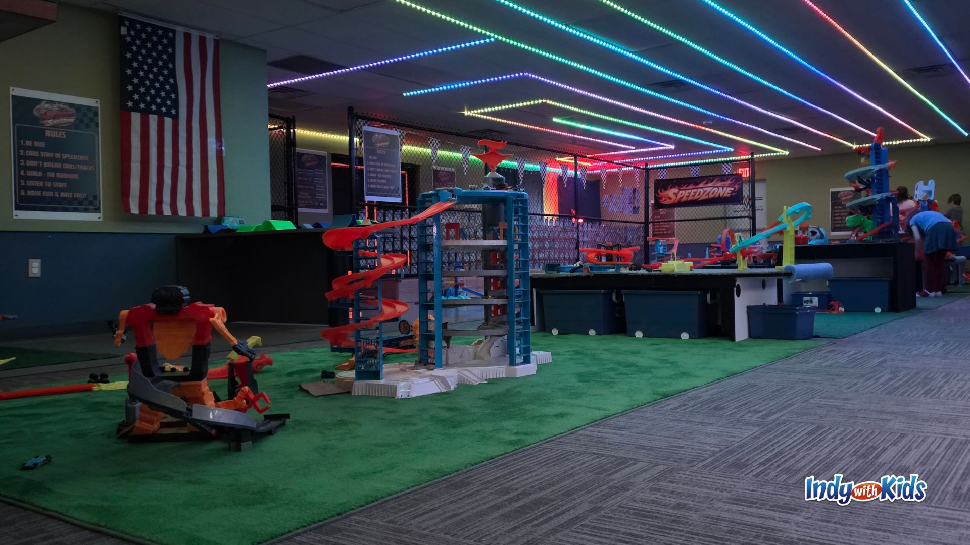 Close-up of Hot Wheels track setup at SpeedZone with race-themed play stations and glowing lights in the background.