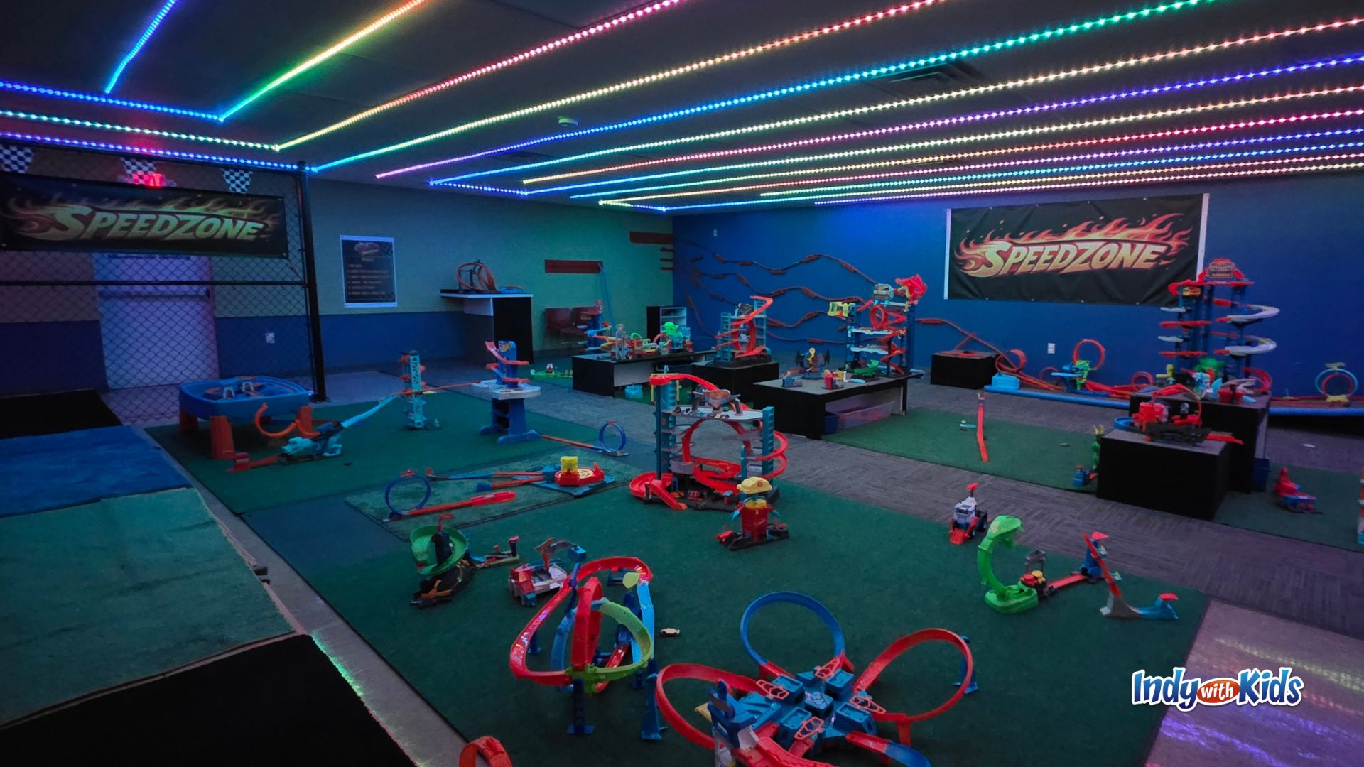 Full overview of SpeedZone indoor race-themed play room with track tables, floor play zones, and colorful ceiling lights.