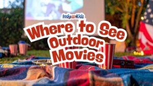 Outdoor movie setup on a blanket with striped popcorn buckets in front of a projection screen at dusk, with an American flag and warm lights nearby. Text overlay reads “Where to See Outdoor Movies.”