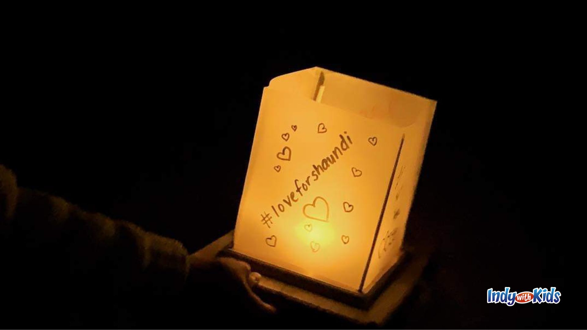 Close-up of a softly glowing paper lantern held at night, decorated with hearts and the handwritten message “#loveforshawndi.”