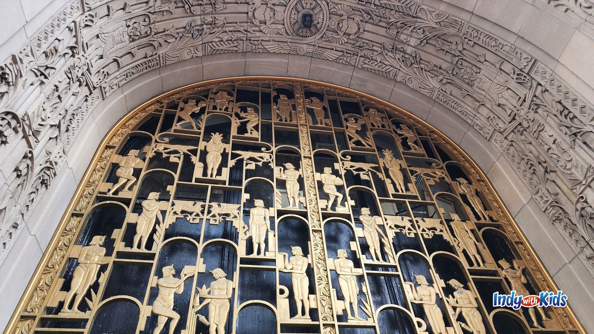 Close-up of decorative gold and black doors on a historic downtown Indianapolis building, surrounded by an elaborate carved stone arch with floral and geometric details.