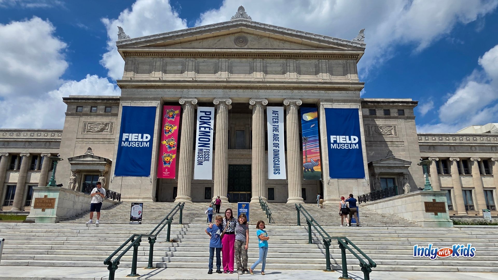 A family stands on the front steps of the Field Museum in Chicago beneath large banners for the Pokémon Fossil Museum exhibition.
