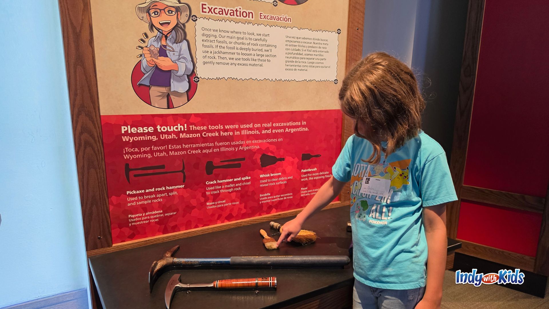 A child wearing a Pokémon shirt explores the Pokémon Fossil Museum exhibition at the Field Museum, touching real excavation tools displayed beneath an educational sign about fossil excavation.
