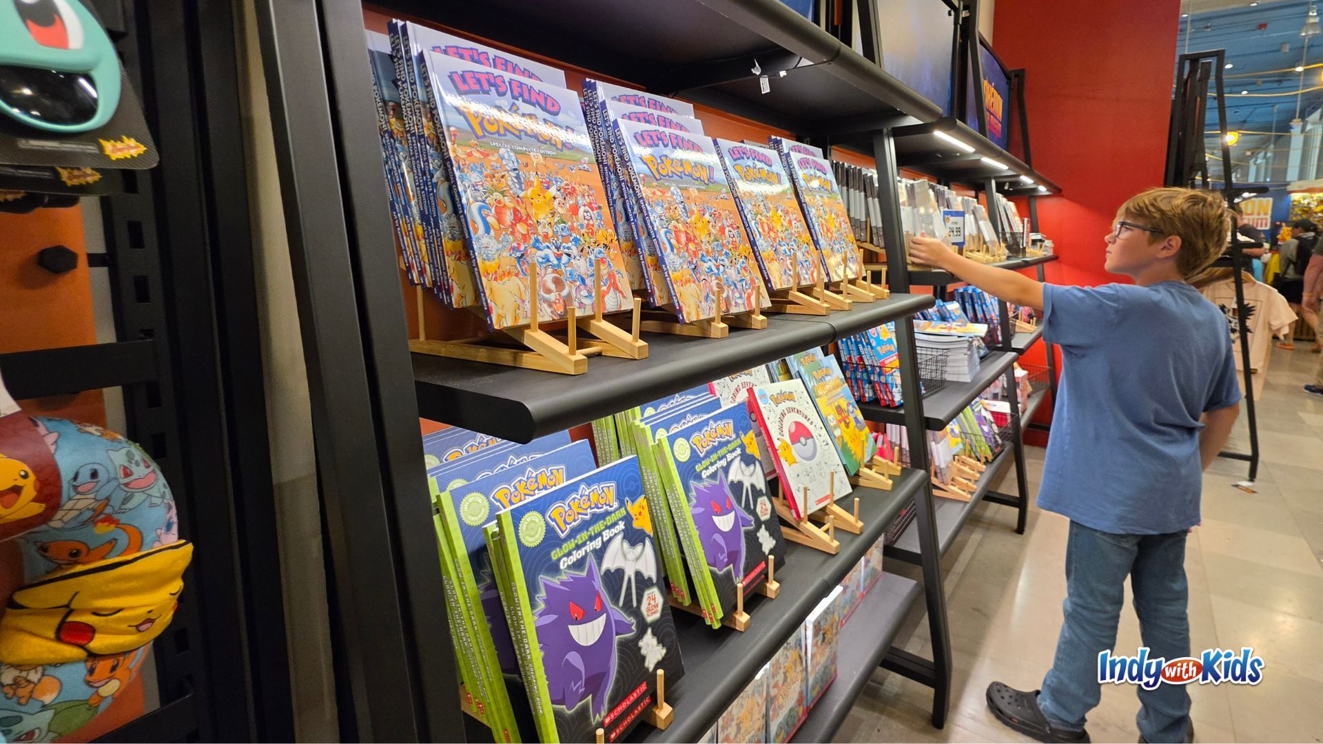 A child browses shelves of Pokémon books, activity books, toys, and merchandise in the Pokemon Merch gift shop.
