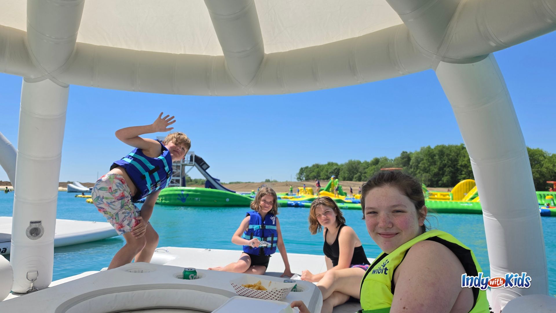 Kids wearing life jackets relax and wave from a floating Aquabana cabana at SKYLAKE Adventure Park.