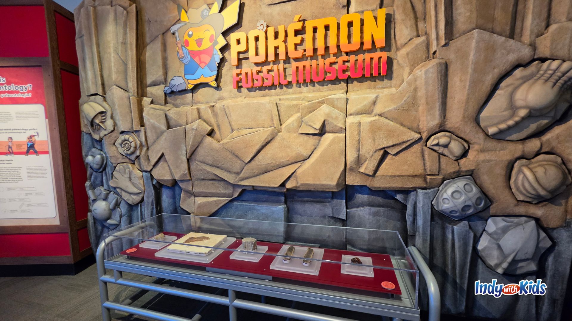 The entrance display for the Pokémon Fossil Museum exhibition at the Field Museum, featuring Excavator Pikachu artwork, fossil-themed walls, and a glass case with fossil specimens.