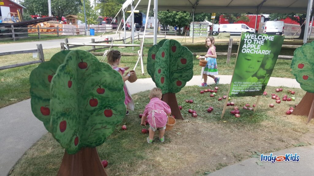 Children in red gingham aprons collect pretend apples from trees at the Little Hands on the Farm apple orchard station during the Indiana State Fair.