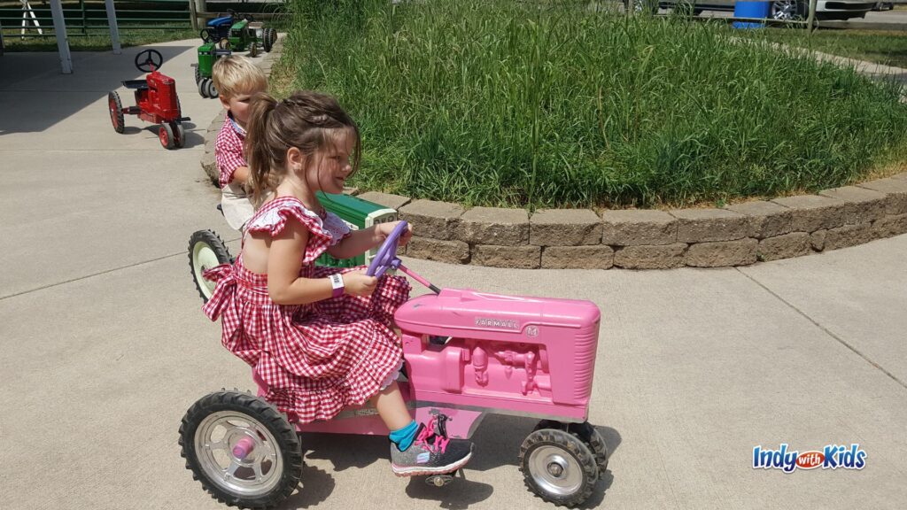 Two children ride small pedal tractors along a path at Little Hands on the Farm during the Indiana State Fair.
